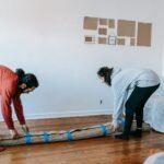 Two adults carefully roll up a rug while packing up in a bright, minimal living room.